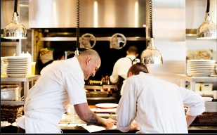 Two chefs in kitchen conversating over menu notes. 