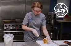 Chef Jessie in the kitchen slicing a biscuit on a cutting board. Chefs of the Mills logo.
