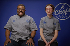 •	Chef Ted and Chef Jessie sitting on stools against a blue backdrop in their grey chef’s coats. Chefs of the Mills logo.