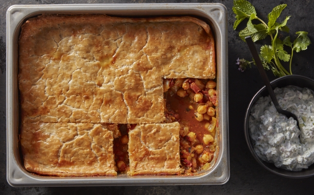 Chana masala pot pie in a pan cut into squares with a side bowl of complimentary sauce.