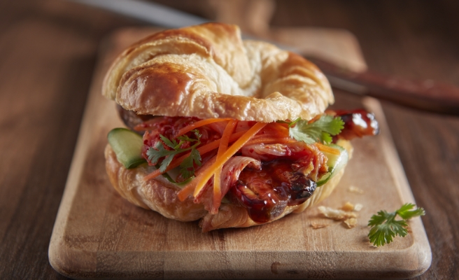 Glazed pork belly in a croissant with cucumbers, kimchi, cilantro and carrots sandwich on a Pillsbury™ croissant.