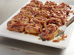 Smoky Caramel Roll recipe on a square white platter being served with a metal spatula.