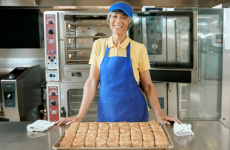 Operator holding a tray of biscuits in a kitchen while smiling