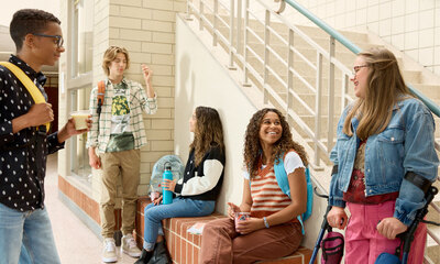 Group of five diverse students talking and smiling in a school hallway.