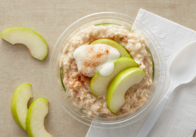 TApple cobbler overnight oats recipe. Yogurt, granola, and oats in a plastic cup with slices of green apple on top.