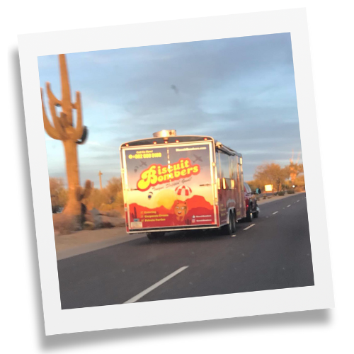 Biscuit bombers food truck traveling down a highway passing a cactus on the side of the road.