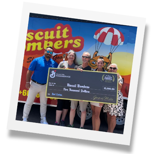 Man and woman holding large check from General Mills Foodservice in front of blue, orange, and yellow Biscuit Bombers food truck.