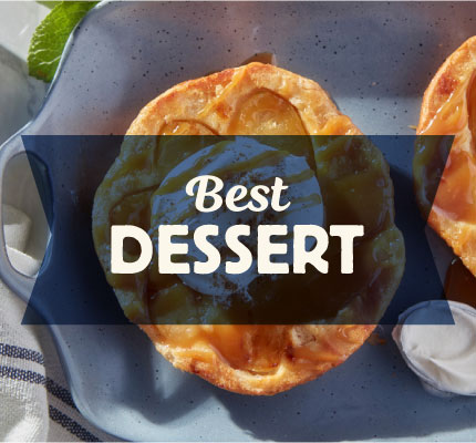 Best dessert. Dark blue transparent ribbon overlays imagery of biscuit dessert with dollop of cream and spoon with cream. Shown in baking tray. Blue and white kitchen towel.