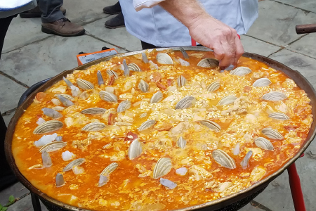 Large pot of paella in outdoor setting showing the hand of catering chef placing clams