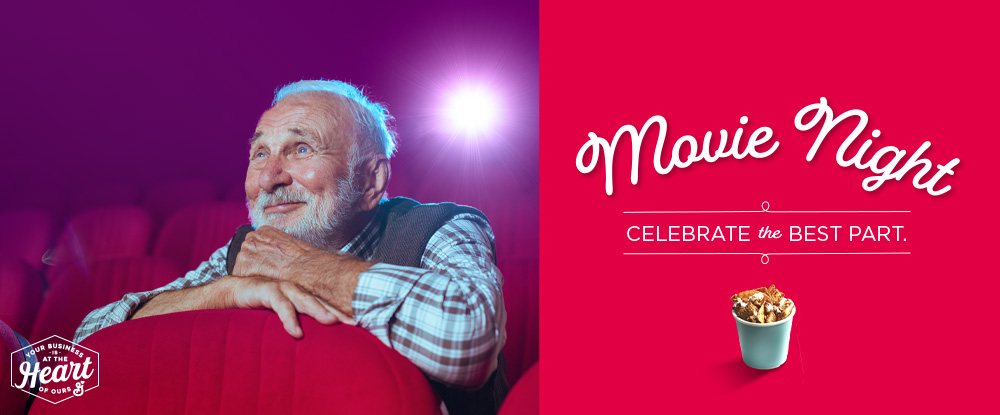 Movie Night. Celebrate the Best Part. Your Business is at the Heart of Ours logo. Snack mix cup on bright red background. Smiling senior man on the edge of his seat in movie theater.